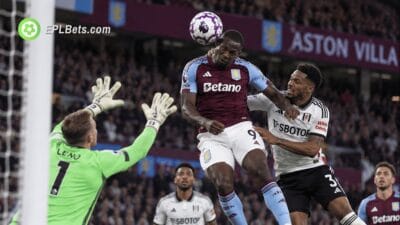 O atacante do Aston Villa, Nicolas Jackson, salta para cabecear a bola sob pressão de um zagueiro do Fulham, enquanto o goleiro Bernd Leno tenta fazer a defesa.