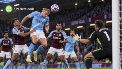 Erling Haaland rises to challenge for a header against Aston Villa defenders as goalkeeper Emiliano Martínez prepares to react during a Premier League match illustration.