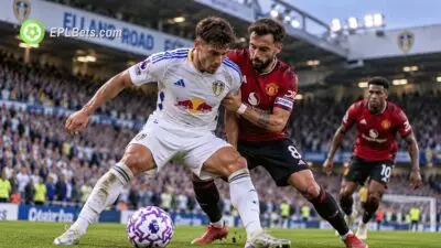 Ilustração de uma partida da Premier League no Elland Road, em que um jogador do Leeds United, com o uniforme branco de casa, protege a bola do capitão do Manchester United, Bruno Fernandes, que veste o uniforme vermelho.