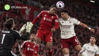 O capitão do Liverpool, Virgil van Dijk, disputa uma cabeçada com um jogador do Arsenal, enquanto o goleiro Alisson Becker tenta alcançar a bola durante uma partida da Premier League em Anfield.
