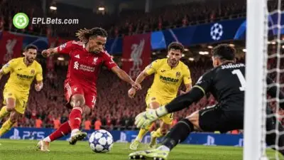 Bradley Barcola in a red Liverpool kit shoots towards goal as the Villarreal goalkeeper attempts to make a save during a Champions League match illustration at Anfield.