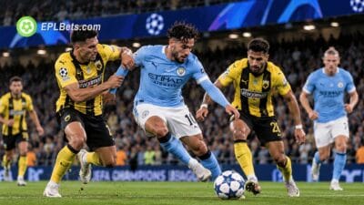 Manchester City midfielder Rayan Cherki dribbles past an AEK Athens defender in yellow and black as another opponent closes in during a Champions League match illustration.